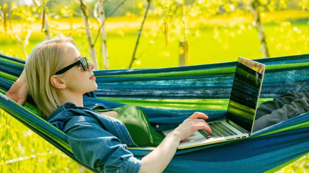 Kobieta leżąca na hamaku z laptopem w otoczeniu natury - symbol równowagi i energii